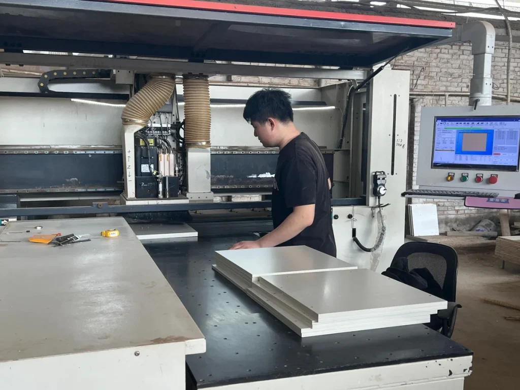 Furniture factory operator preparing matching cabinet panels at a cutting machine