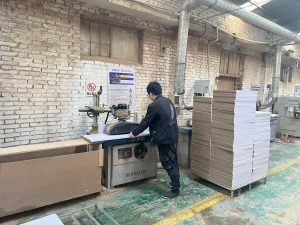 Worker handling cabinet panels beside a woodworking machine in a furniture workshop