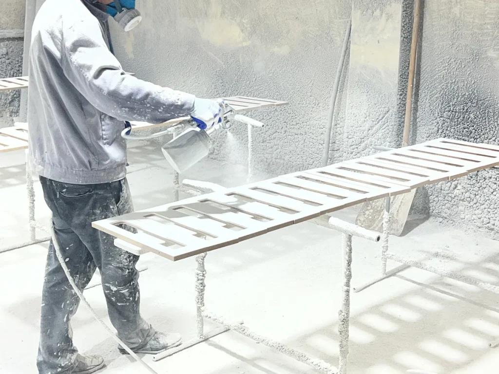 Factory worker applying a white finish to furniture panels in a controlled spray area